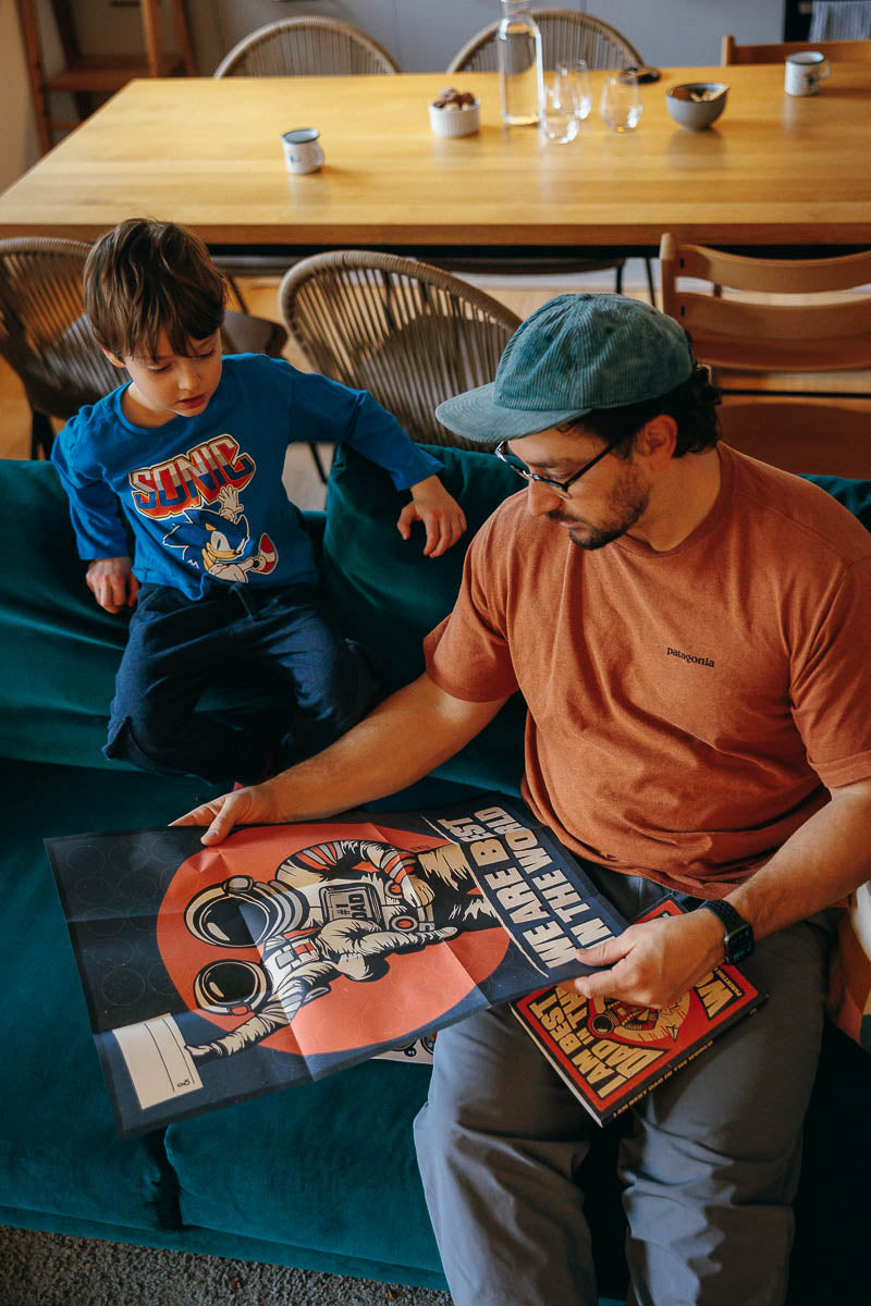 Man and child looking at the stickers and poster together in a cozy indoor settings from the I AM BEST Dad in the world book pack.