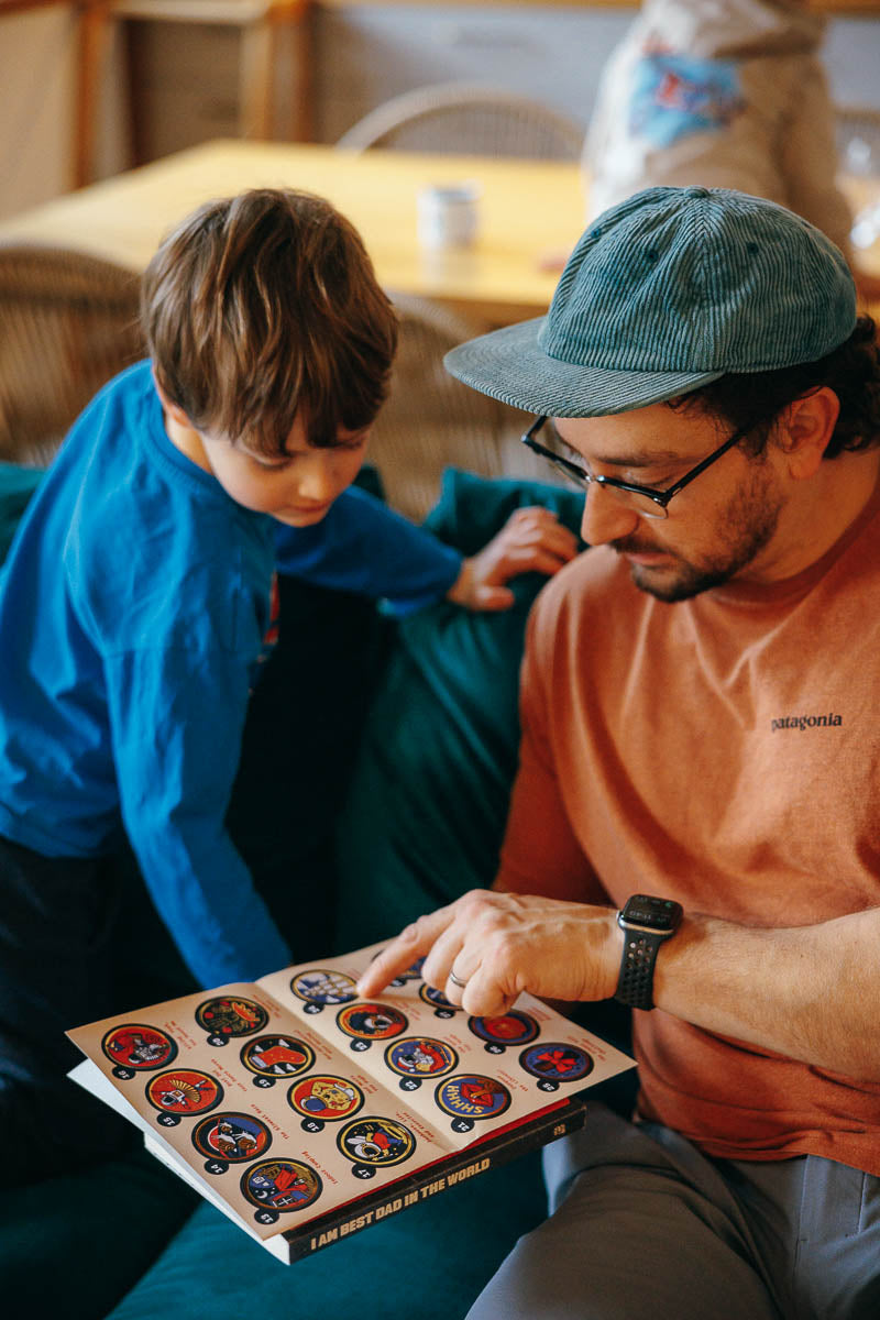 Man and child looking at the stickers in a cozy indoor settings from the I AM BEST Dad in the world book pack.